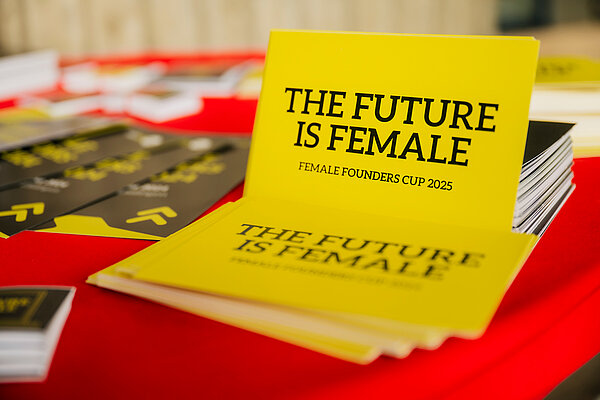 Es liegen mehrere Postkarten auf einem Tisch mit rotem Untergrund. Text: THE FUTURE IS FEMALE, FEMALE FOUNDERS CUP 2025.