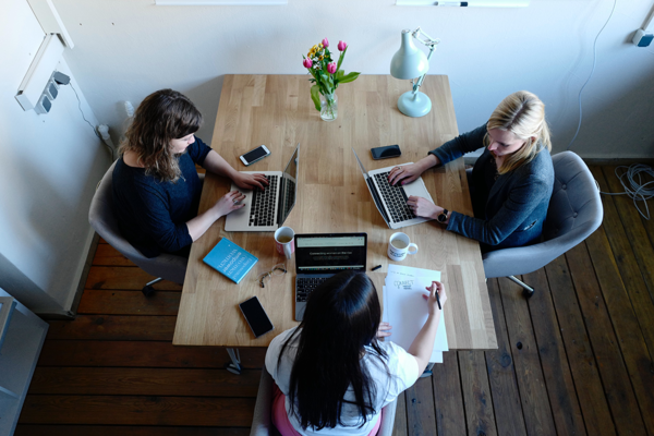 Drei Frauen sitzen vor Laptops an einem Konferenztisch in einer Arbeitssituation.